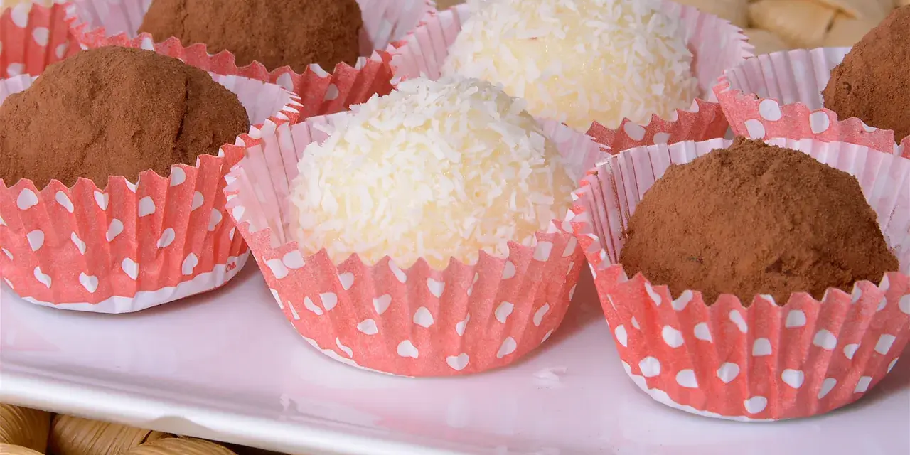 Deliciosas trufas de coco y chocolate, algunas cubiertas de coco rallado y otras de cacao en polvo, presentadas en capacillos rojos con puntos blancos.