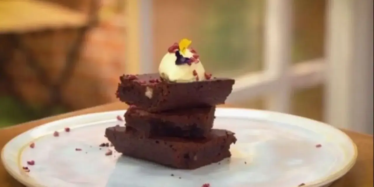 Delicioso brownie airfryer apilado, coronado con helado y pétalos.