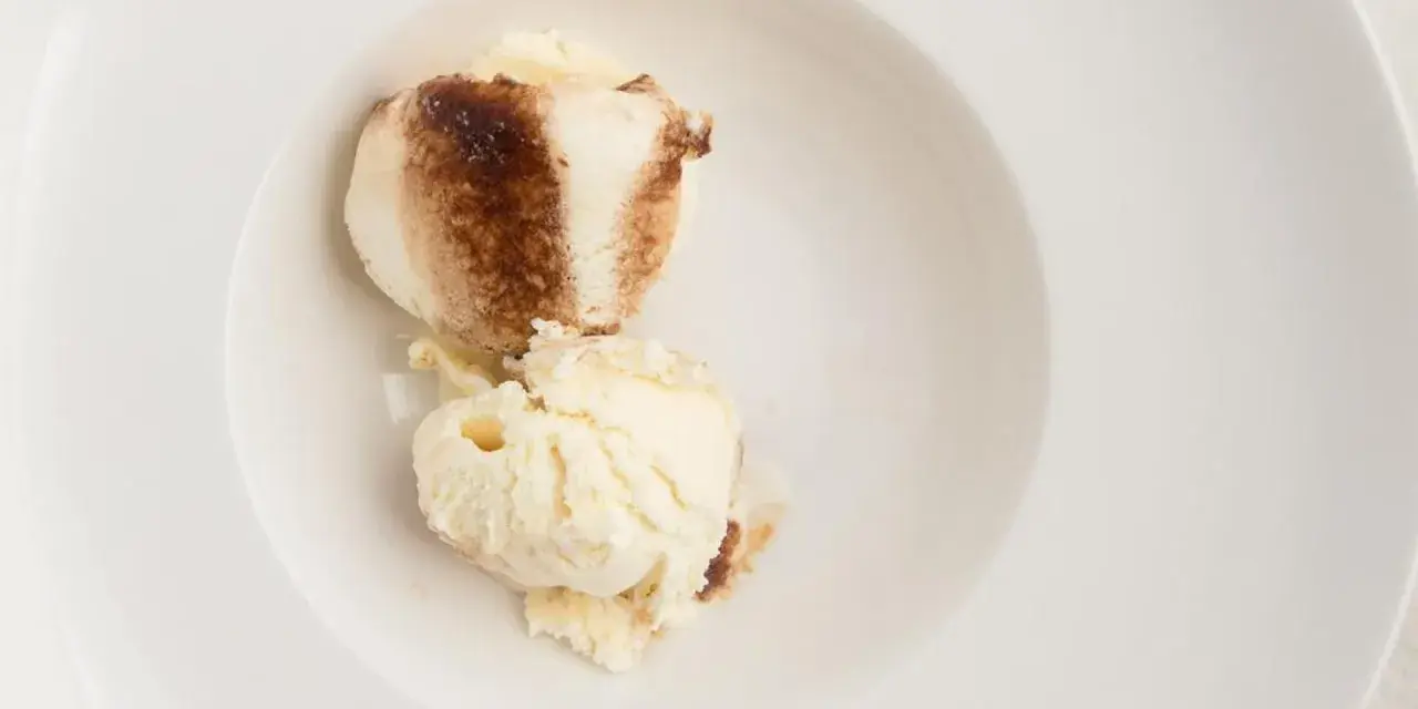 Dos bolas de helado de tiramisú con un toque de cacao en polvo en un cuenco blanco.