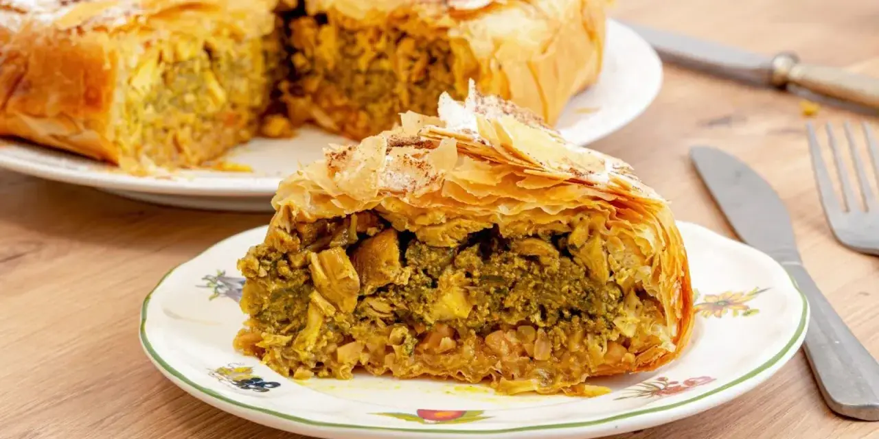 Pastela marroqui, un pastel salado de hojaldre relleno de pollo y especias, servido en un plato decorado.