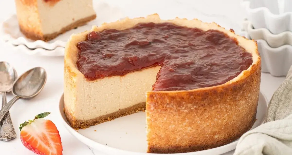 Tarta de queso vegana con cobertura de fresa, cremosa y deliciosa. Una porción ya cortada muestra su interior.