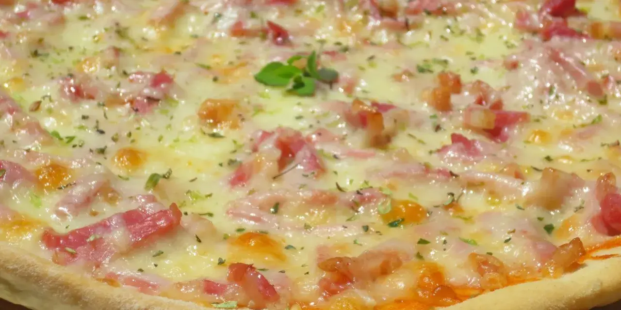 Pizza con masa hecha en Thermomix, cubierta de queso fundido, trocitos de bacon y hierbas aromáticas.