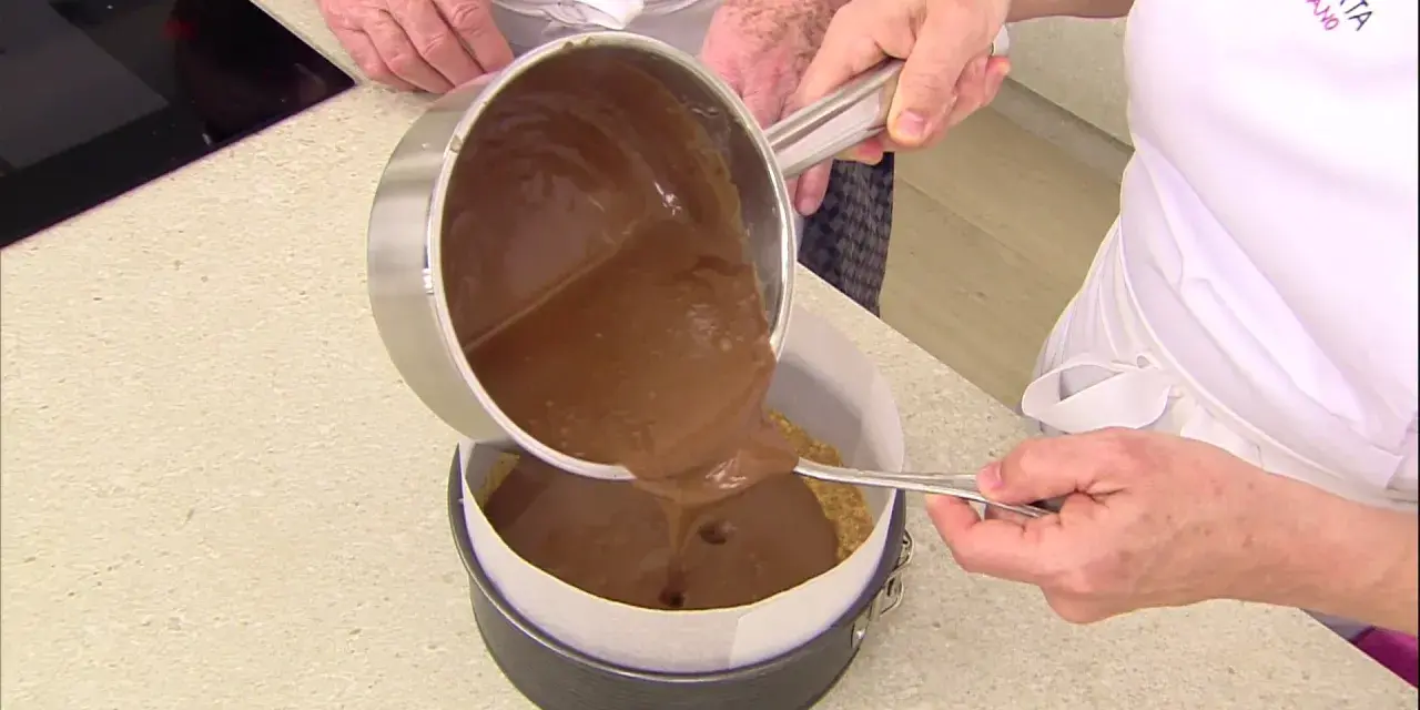 Vertiendo cobertura de chocolate sobre una base de galleta para un delicioso pastel de chocolate.