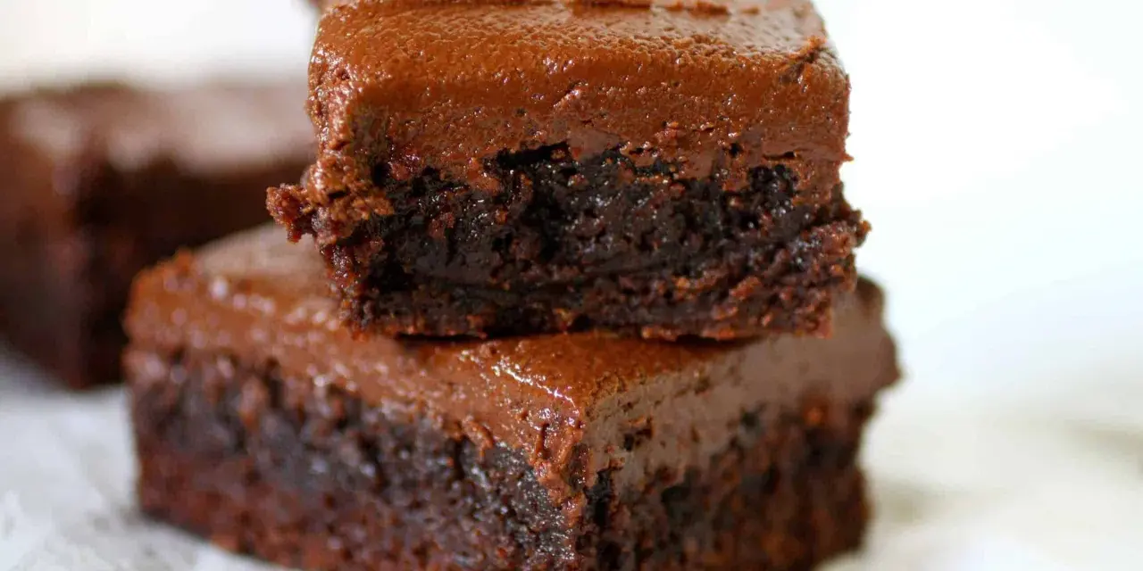 Dos deliciosos brownies con nueces apilados, cubiertos con glaseado de chocolate cremoso.