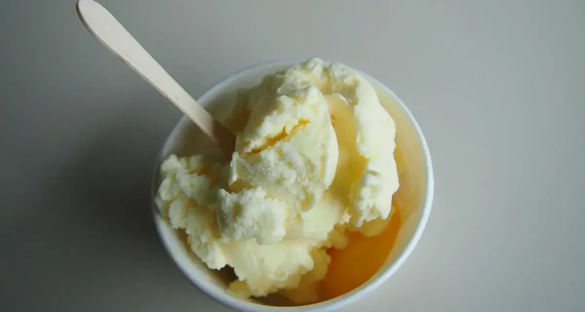 Un cremoso helado de melón en un cuenco blanco, listo para ser disfrutado con su cuchara de madera.