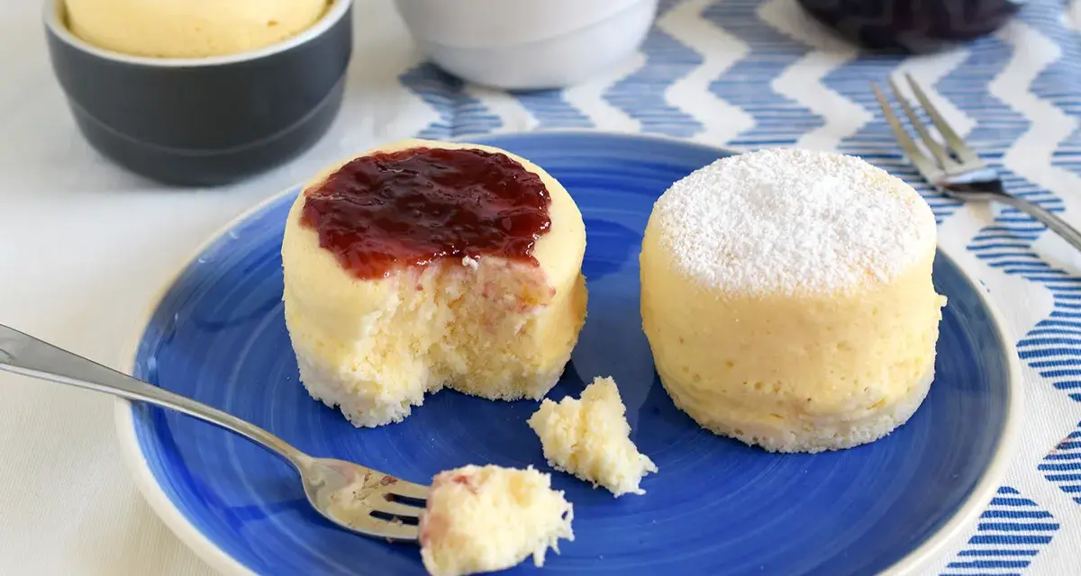 Dos bizcochos de microondas en un plato azul. Uno tiene mermelada de fresa y el otro azúcar glas.