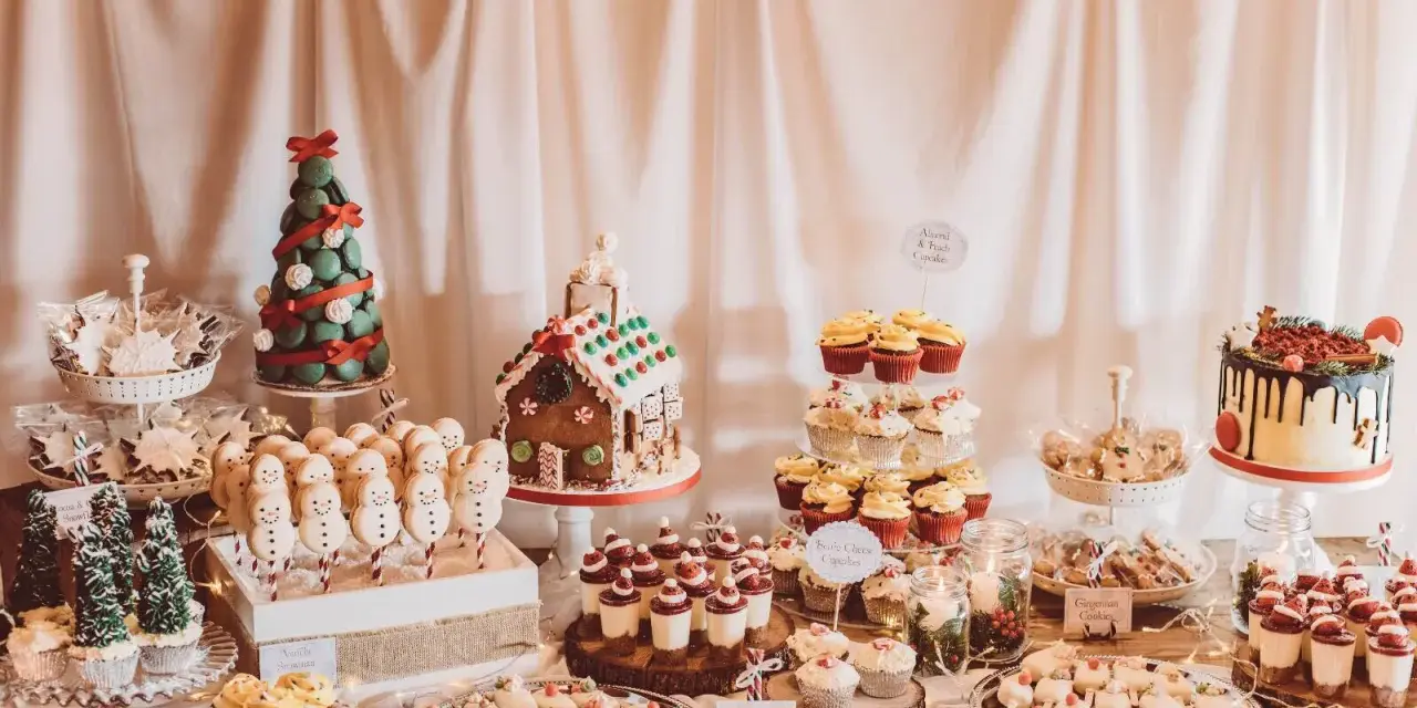 Mesa llena de postres navideños: árbol de macarons, casa de jengibre, muñecos de nieve, cupcakes y galletas.