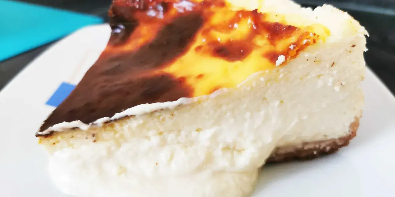 Porción de chese cake con borde quemado y relleno cremoso, servida en plato blanco.
