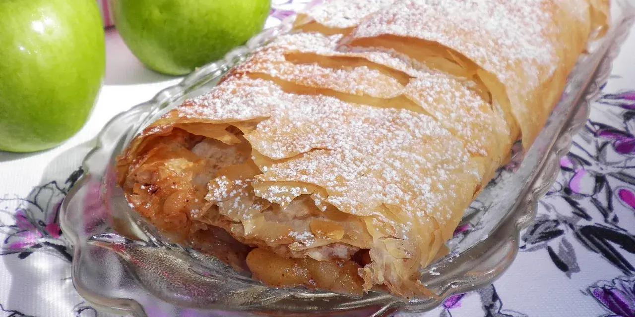 Delicioso strudel de manzana recién horneado, espolvoreado con azúcar glas y acompañado de manzanas verdes frescas y canela.