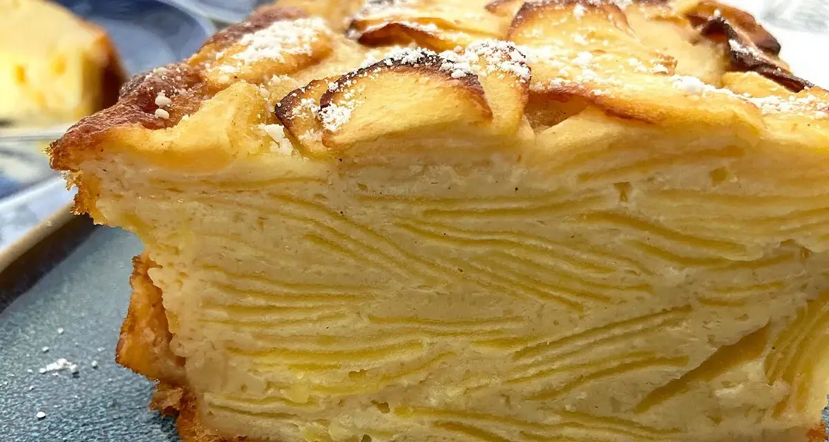 Un trozo de pastel de capas con trozos de manzana en la parte superior, espolvoreado con azúcar glas. Un postre invisible aux pommes.