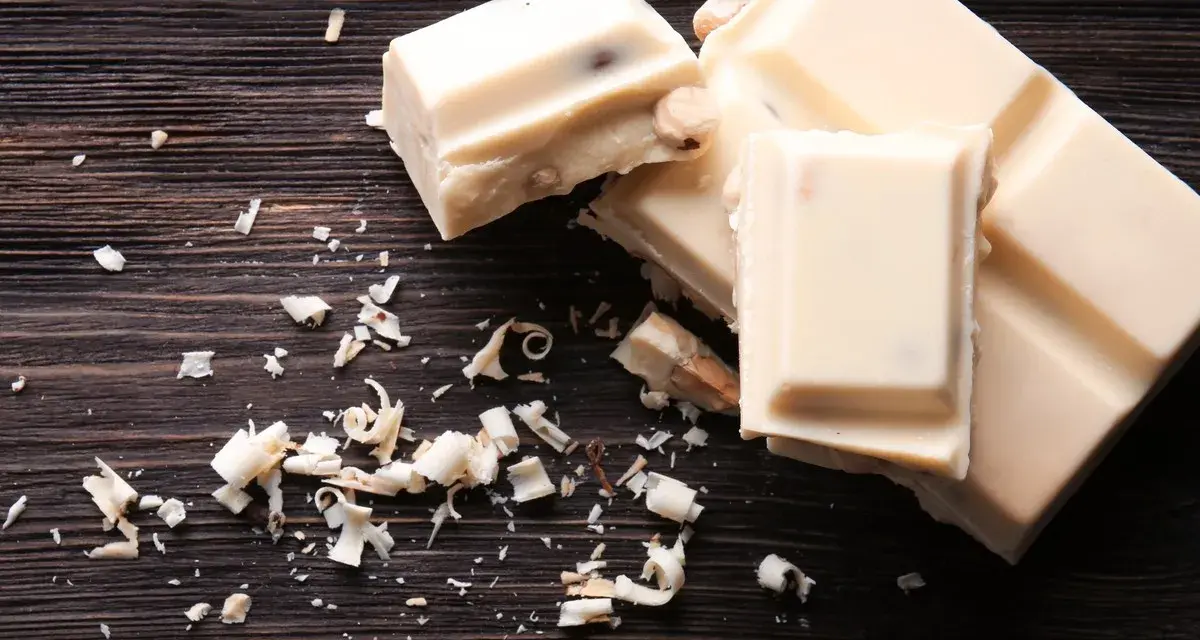 Deliciosos postres con chocolate blanco, trozos y virutas esparcidos sobre una tabla de madera oscura.
