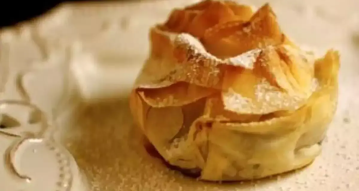 Delicioso saquito de pasta filo relleno de queso, espolvoreado con azúcar glas sobre un plato blanco.