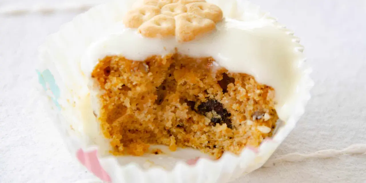 Un muffin de zanahoria con glaseado blanco y una galleta decorativa en forma de flor.