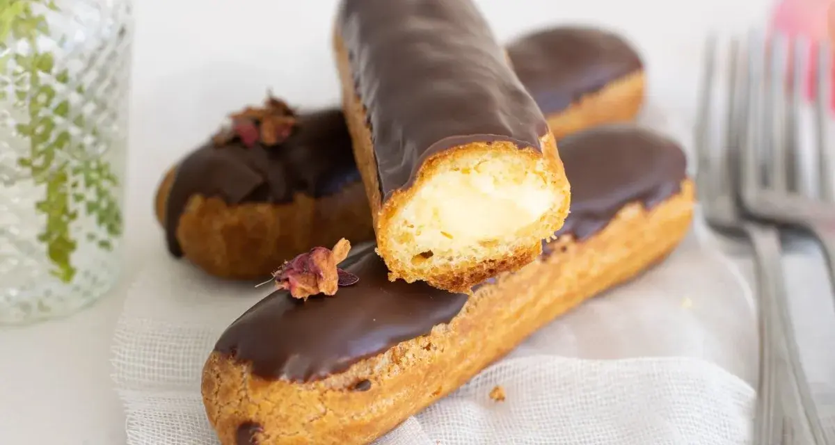Pastel eclair cubierto de chocolate, relleno de crema. Decorado con pétalos secos.