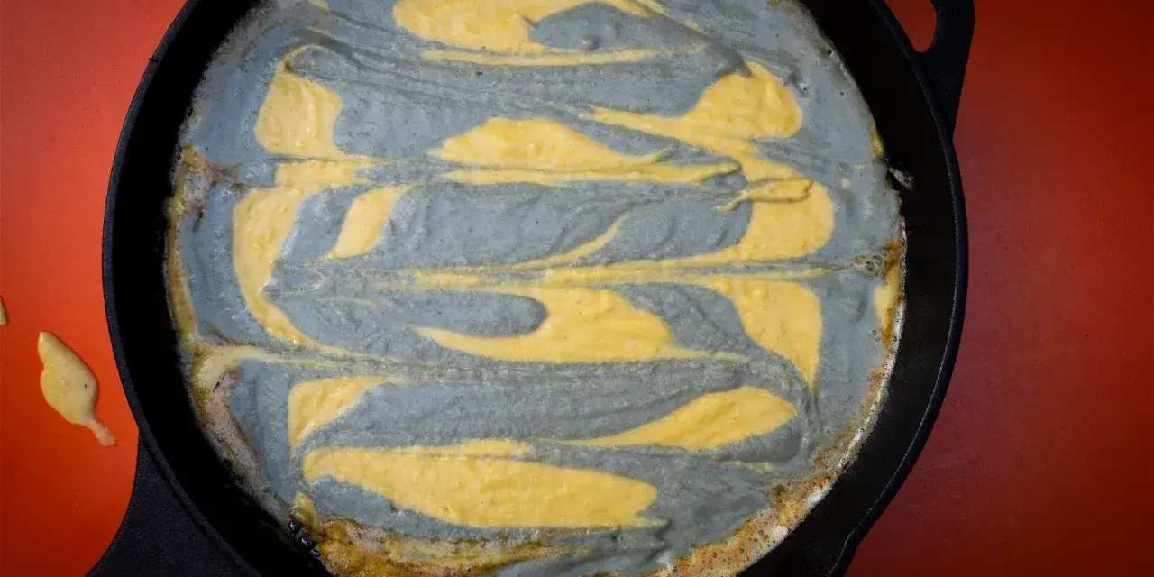 Pastel de maíz con remolinos grises y amarillos en una sartén de hierro fundido.