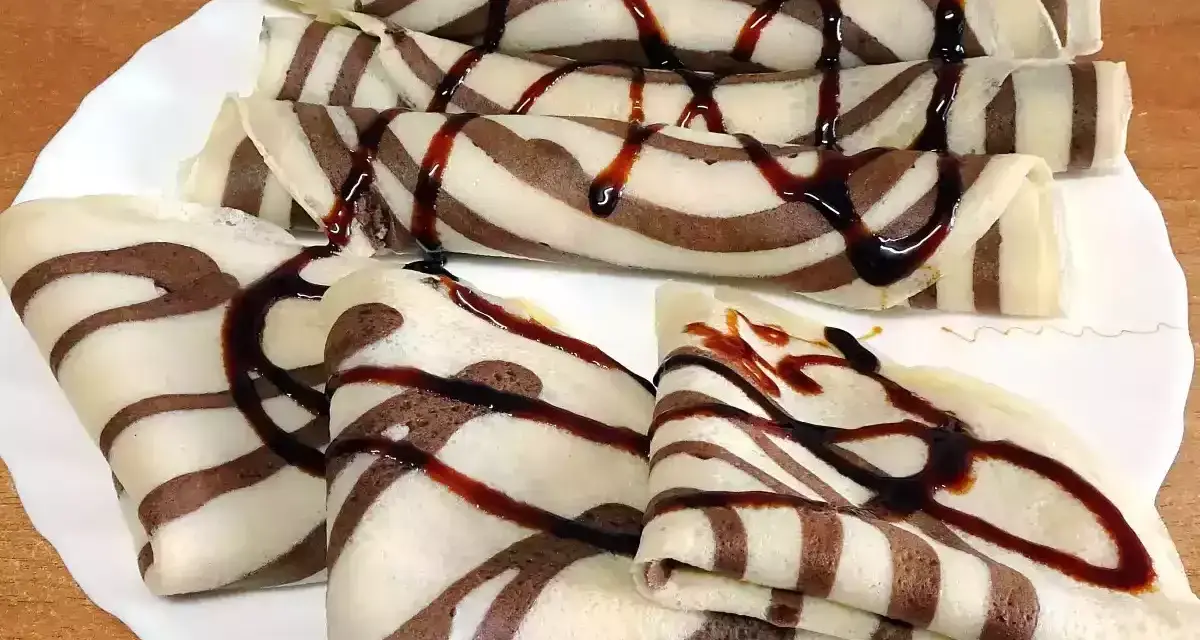 Deliciosos crepes de chocolate rayados, enrollados y doblados, cubiertos con sirope de chocolate.