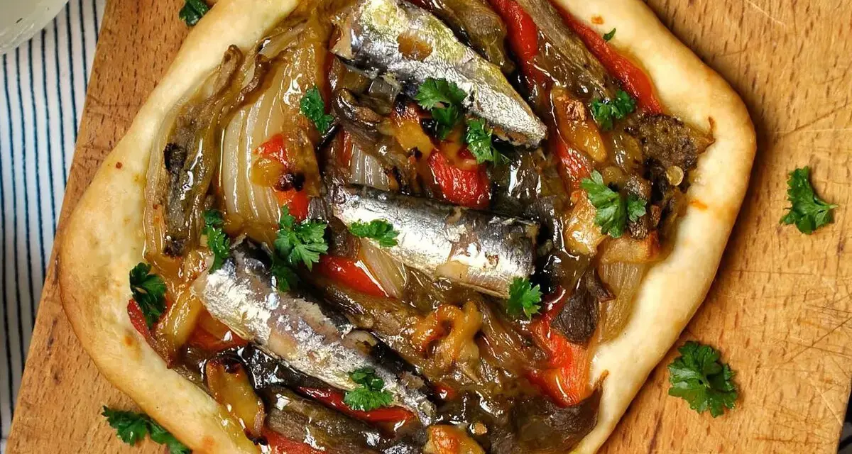 Coca de recapte con verduras asadas y sardinas, decorada con perejil fresco.