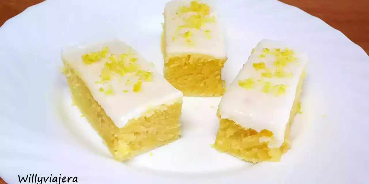Tres porciones de brownie de limón con glaseado blanco y ralladura de limón, servidas en un plato blanco.