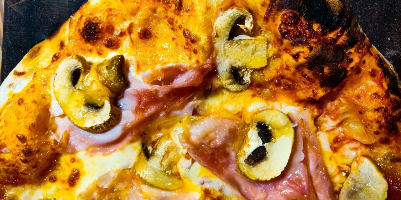 Pizza masa madre con champiñones y jamón, con bordes dorados y burbujas de queso fundido.