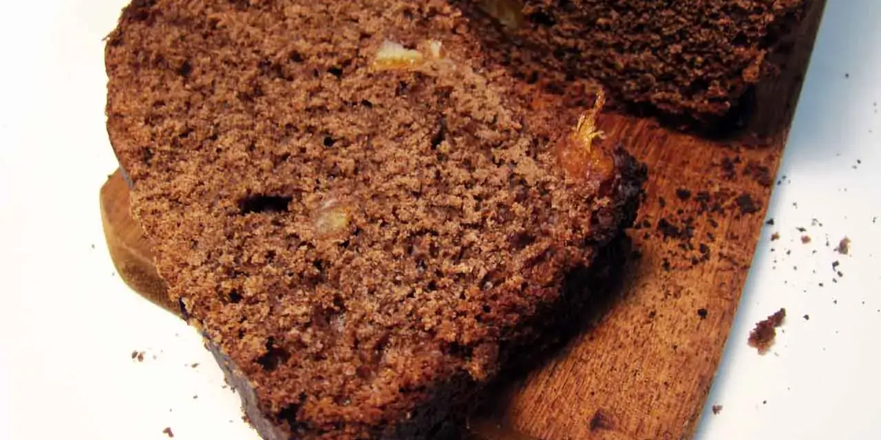 Rebanadas de pan de chocolate húmedo y denso, con trozos de fruta confitada, servidas en una tabla de madera.