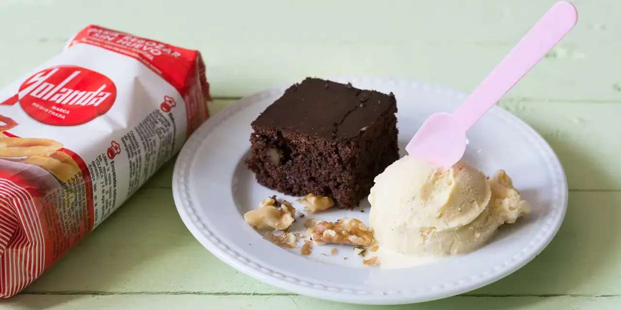 Un delicioso brownie sin huevo con helado de vainilla y nueces, junto a un paquete de Yolanda.