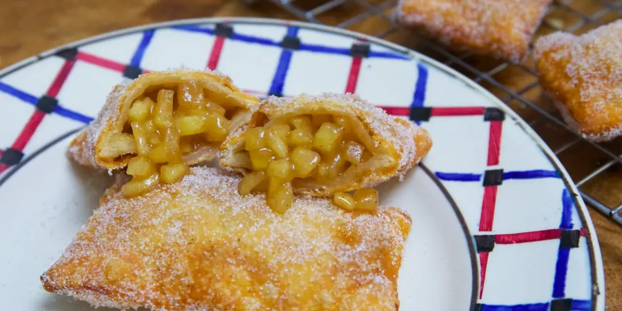 Empanada de manzana recién hecha, dorada y espolvoreada con azúcar. Una está partida, mostrando el relleno jugoso de manzana.