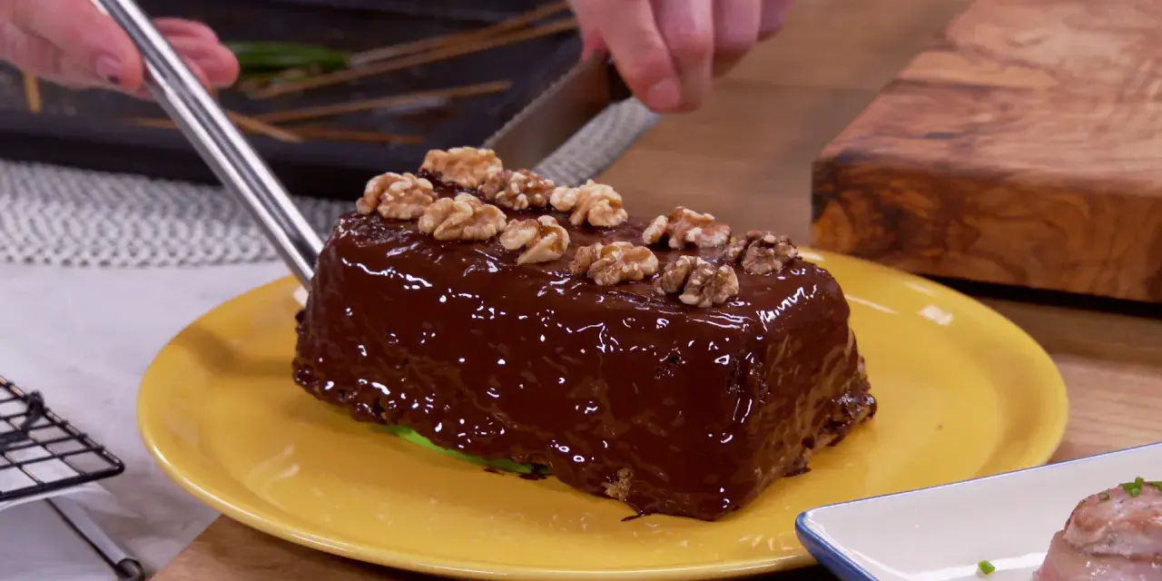 Un delicioso bizcocho de plátano cubierto de chocolate brillante y nueces, listo para ser cortado.