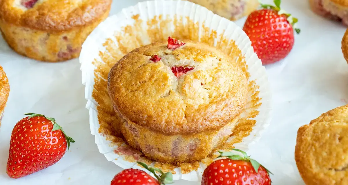 Delicioso postre con fresas, muffins dorados con trozos de fresa y fresas frescas alrededor.
