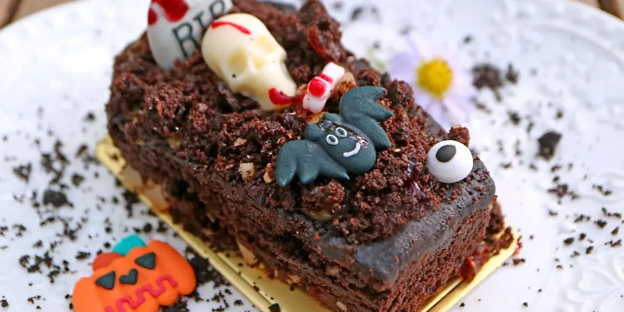 Tartas de Halloween originales: un pastel de chocolate cubierto de tierra de galleta, con un cráneo, un murciélago y una lápida.