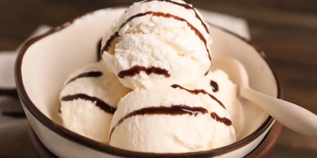 Cuatro bolas de helado de chocolate blanco con sirope de chocolate en un cuenco.