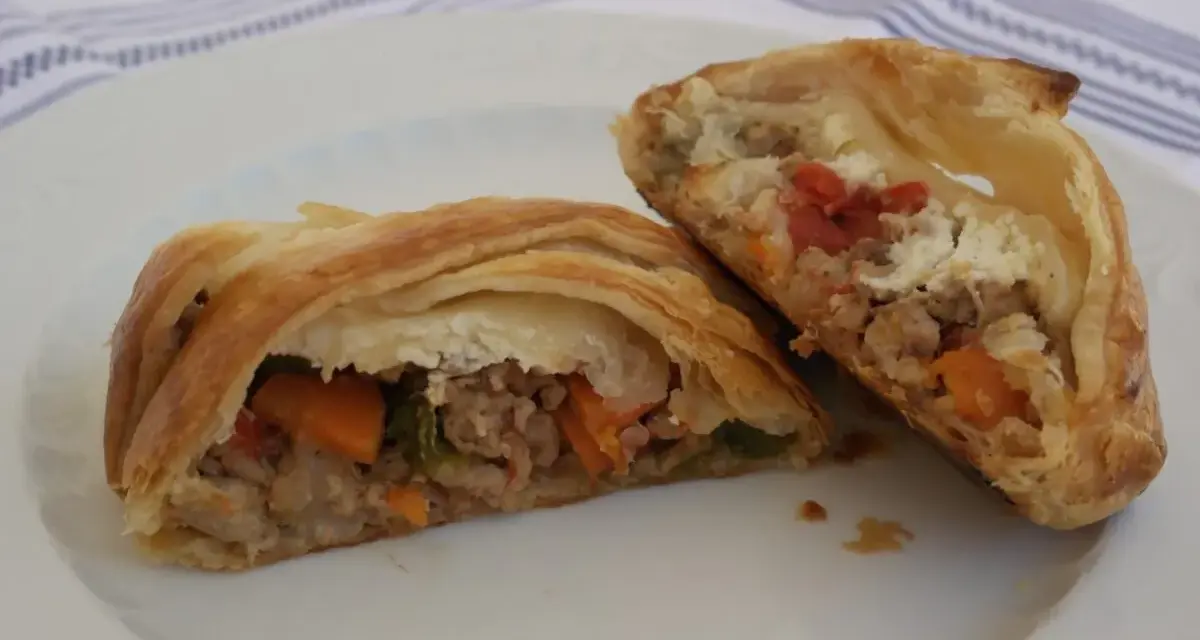 Hojaldre con carne picada y verduras, cortado por la mitad, mostrando el relleno jugoso.