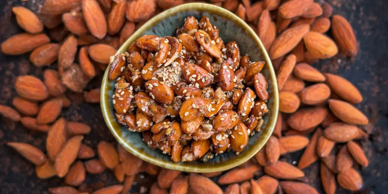 Un cuenco lleno de almendras caramelizadas, cubiertas de semillas de sésamo, rodeadas de almendras enteras.