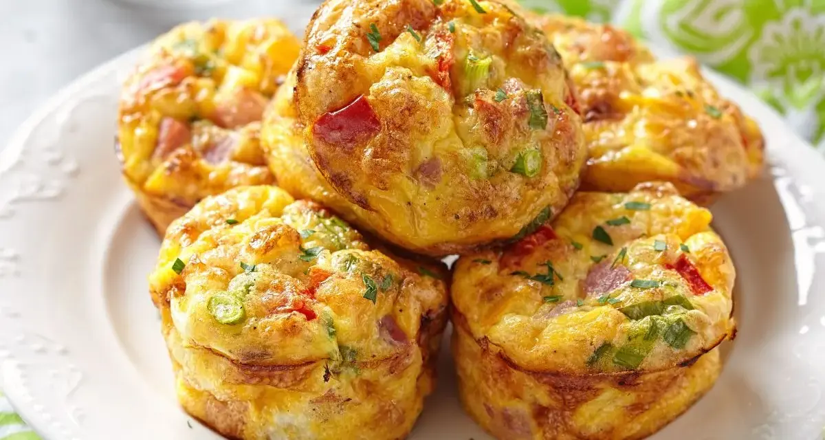 Montón de muffins saludables con huevo, pimiento rojo, cebolleta y jamón, espolvoreados con perejil.