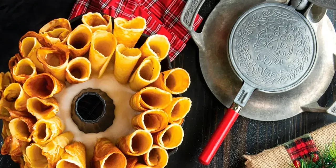 Deliciosos postres noruegos en forma de conos dorados, listos para rellenar. Una vieja gofrera de hierro reposa cerca.