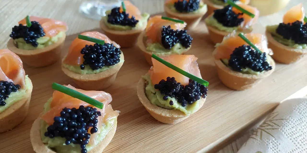 Deliciosas tartaletas de salmón y aguacate, coronadas con caviar negro y cebollino. Un bocado elegante y sabroso.
