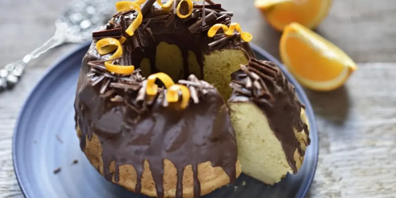 Bizcocho de chocolate y naranja, cubierto con glaseado de chocolate, virutas de chocolate y cáscara de naranja.