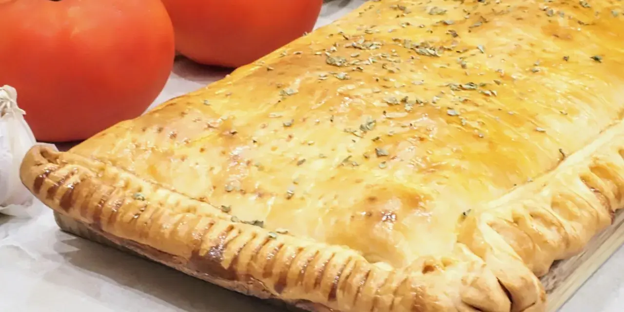 Empanada de pisto dorada y crujiente, con tomates frescos y ajo al lado. ¡Un manjar casero!