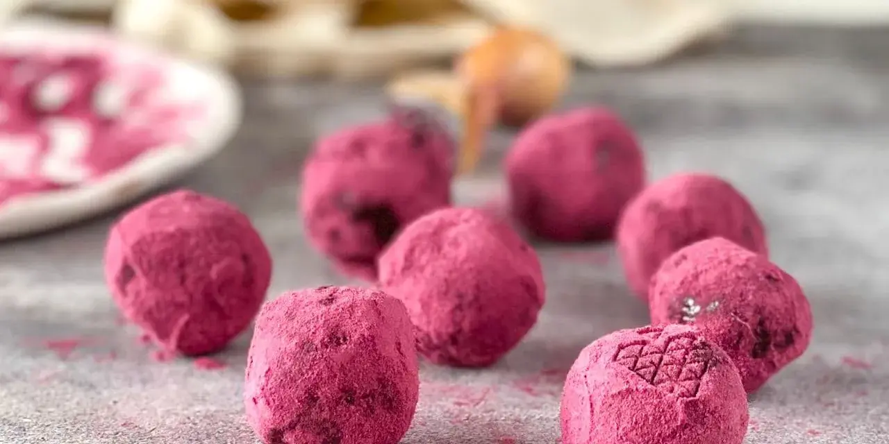 Deliciosas trufas de chocolate cubiertas de polvo rosa vibrante, algunas con un patrón grabado.