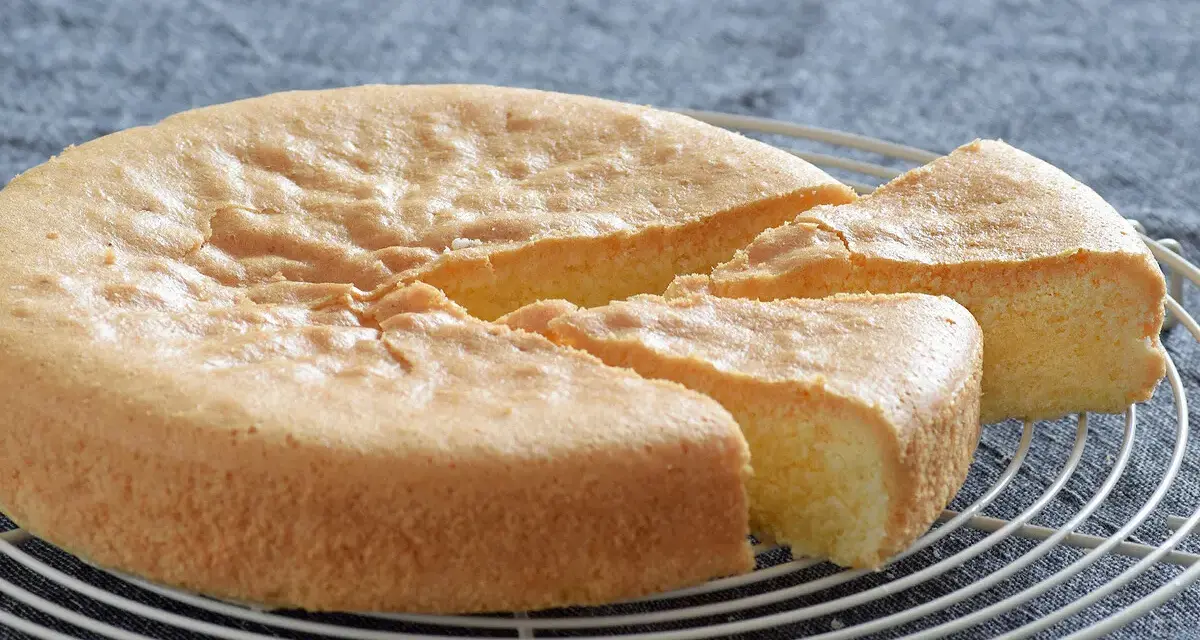 Un esponjoso bizcocho sin gluten, recién horneado y cortado en porciones, descansa sobre una rejilla.