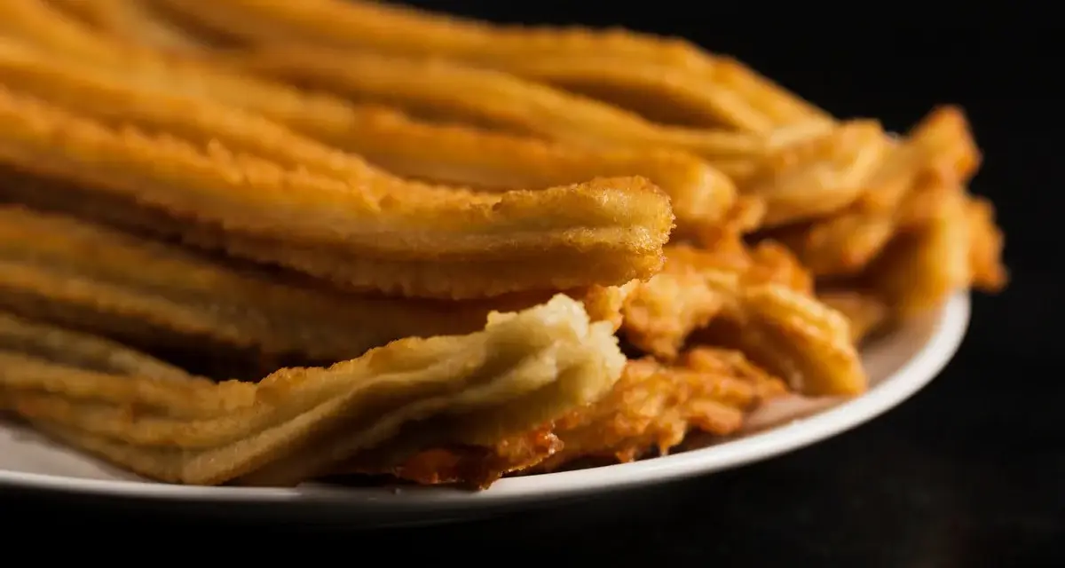 Montón de churros de patata dorados y crujientes apilados en un plato blanco.
