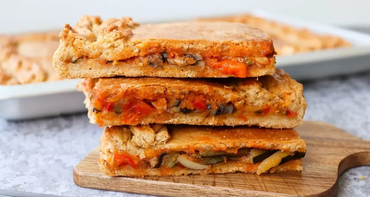 Tres porciones de empanada de verduras apiladas, mostrando el relleno de pimientos, calabacín y tomate.