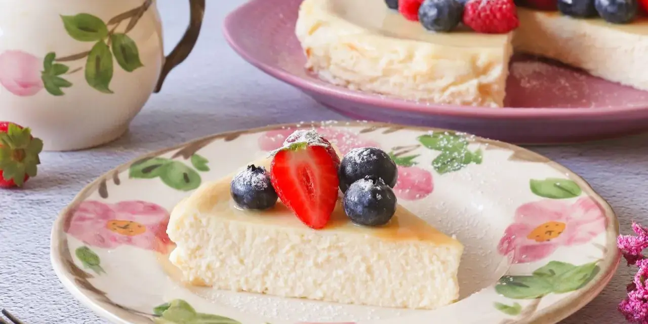 Deliciosa tarta de requesón, decorada con fresas y arándanos, servida en un plato floral.