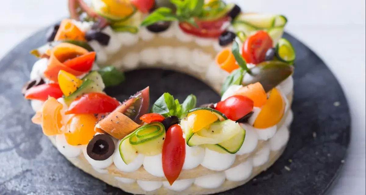 Deliciosa cream tart circular adornada con tomates, pepino, aceitunas y albahaca.