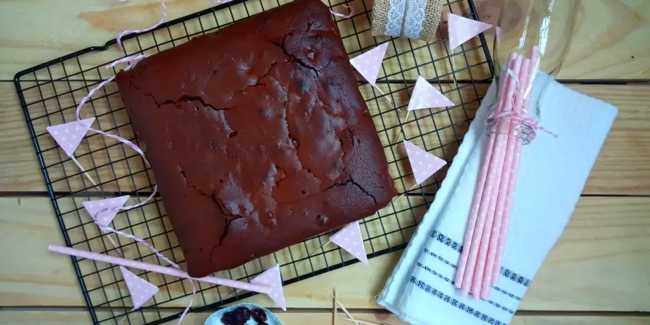 Un delicioso brownie recién horneado, listo para ser cortado. Decorado con banderines rosas y arándanos.