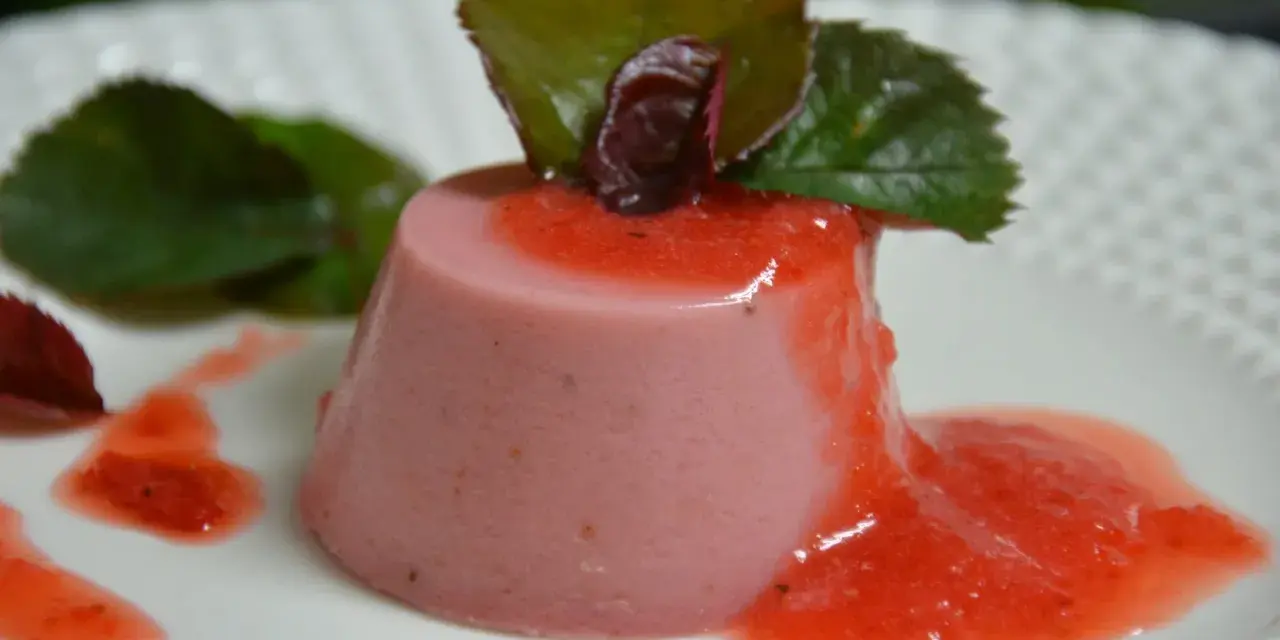Delicioso panna cotta de fresa, bañado en salsa de fresa y decorado con hojas verdes.