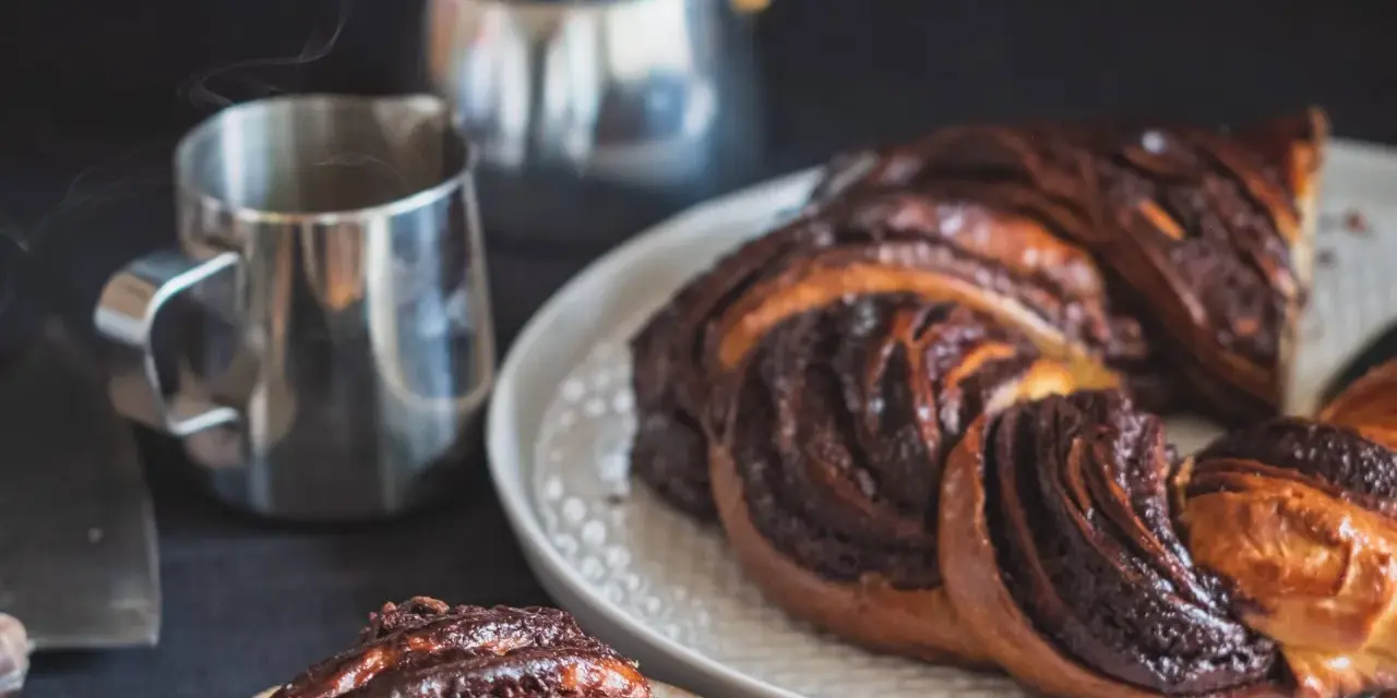 Deliciosa trenza de chocolate recién horneada, humeante junto a una taza de café.