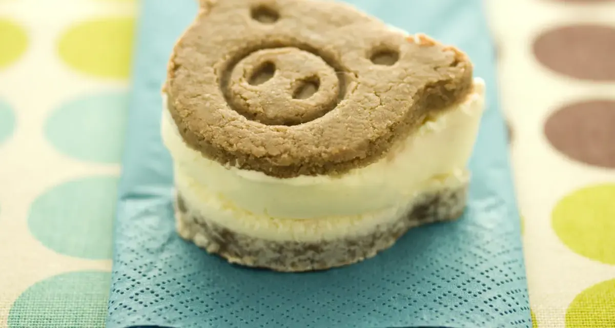 Un delicioso helado de galleta con forma de cerdito, servido sobre una servilleta azul turquesa.