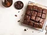 Delicioso brownie sin horno, cortado en cuadrados y espolvoreado con sal marina. Ingredientes como cacao y chocolate en trozos acompañan esta tentación.