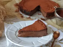 Una rebanada de torta de chocolate, cubierta de cacao en polvo, reposa en un plato blanco. El postre se ve cremoso y delicioso.