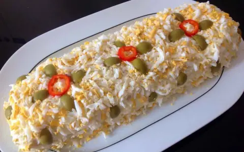 Brazo de gitano de patata cubierto de huevo duro rallado, aceitunas verdes y rodajas de pimiento rojo.